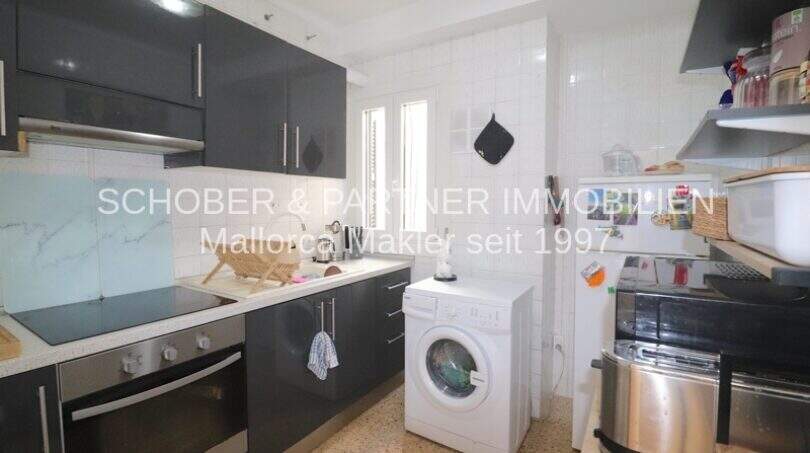 Cocina con frentes de alto brillo oscuro, horno empotrado, placa vitrocerámica y lavadora en apartamento Porto Cristo