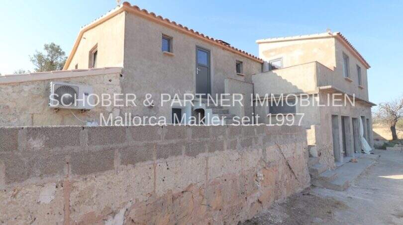 Außenansicht eines sanierten Landhauses in Portocristo mit Natursteinmauer, Terrakottadach und Klimaanlage.