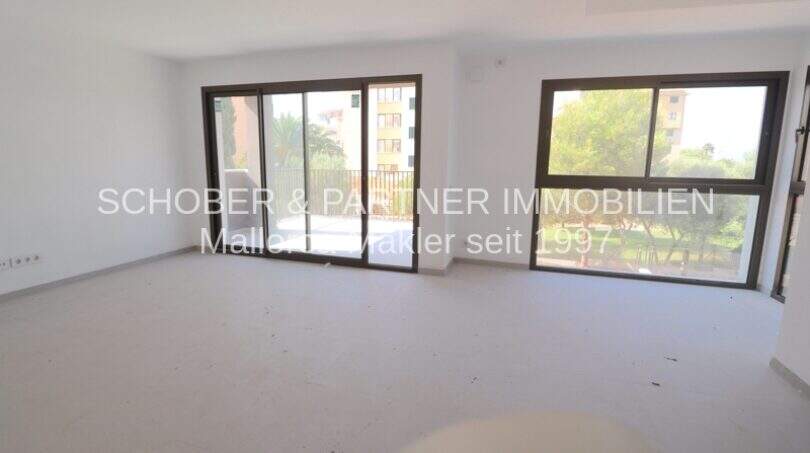 Espacio habitable luminoso y vacío con grandes ventanales panorámicos y acceso al balcón en el apartamento de nueva construcción en Cala Millor.