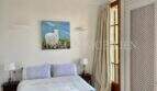Dormitorio luminoso con cama doble, colcha azul, ventanas de madera y cuadro decorativo de ovejas en apartamento del casco antiguo de Palma
