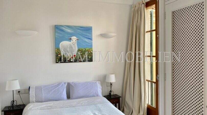 Dormitorio luminoso con cama doble, colcha azul, ventanas de madera y cuadro decorativo de ovejas en apartamento del casco antiguo de Palma