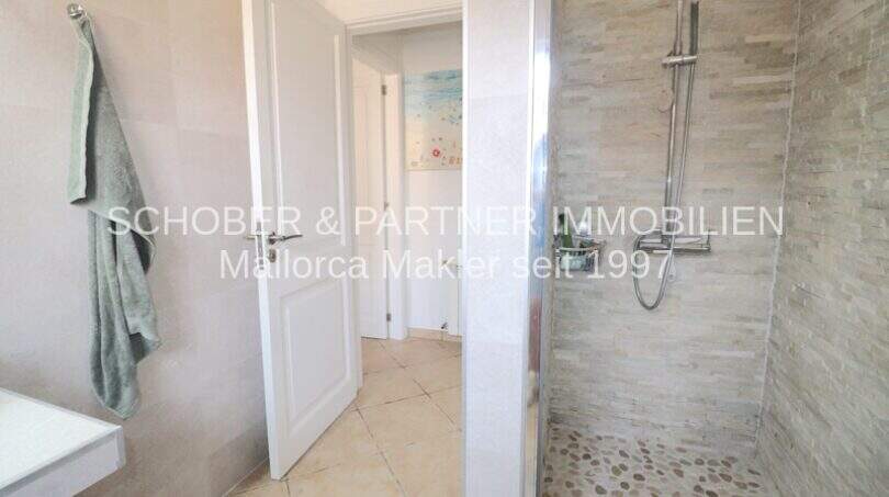 Modern bathroom with natural stone shower, glass partition and towel hooks in Villa Son Servera with sea view.