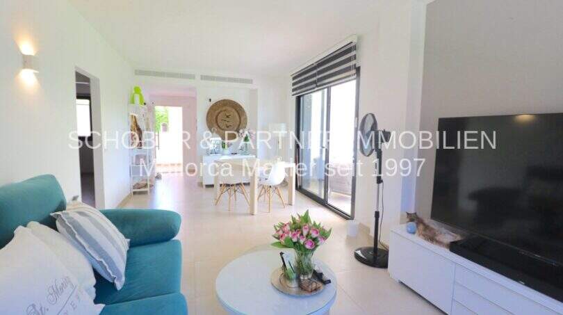 Helles Wohnzimmer mit türkisem Sofa, großem TV und Zugang zur Terrasse in hochwertiger Eckwohnung Sa Coma