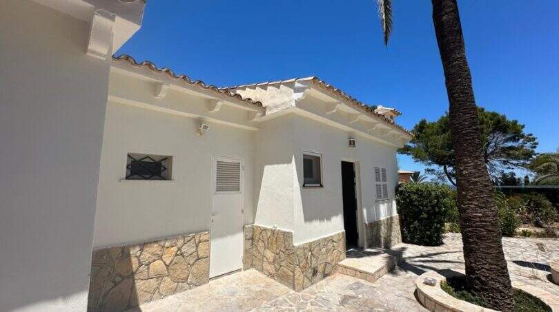 Außenbereich der mediterranen Villa in Cala Murada mit weißer Fassade, Natursteinverkleidung und Palme.