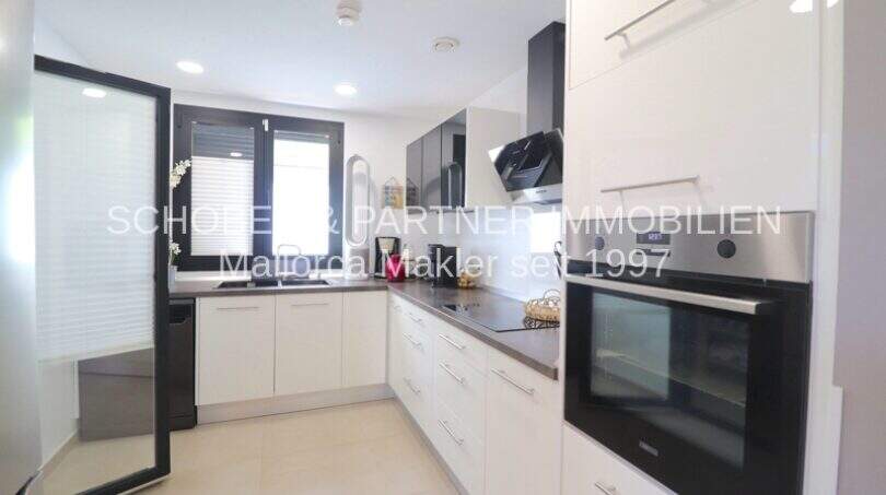 Moderne weiße Einbauküche mit Zanussi-Backofen, Induktionskochfeld und Fenster in Wohnung Sa Coma