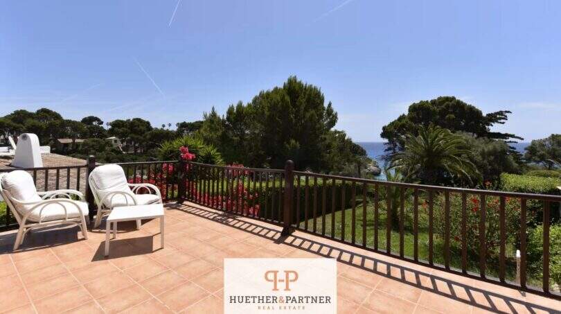 Terraza soleada de la planta baja en Cala Mandia con vista al mar, muebles de ratán y exuberante jardín.