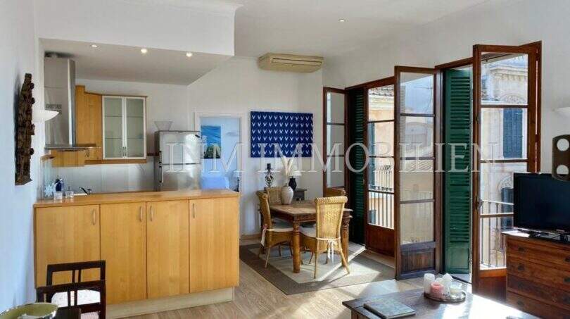 Cocina abierta con frente de madera, mesa de comedor y balcón con contraventanas verdes en apartamento del casco antiguo de Palma