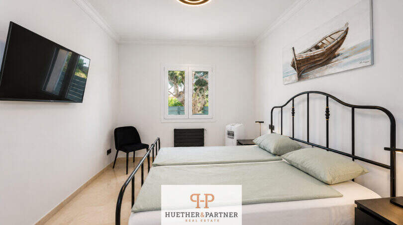 Helles Schlafzimmer der Villa Sa Torre mit zwei Einzelbetten, TV und Wandbild eines Bootes.
