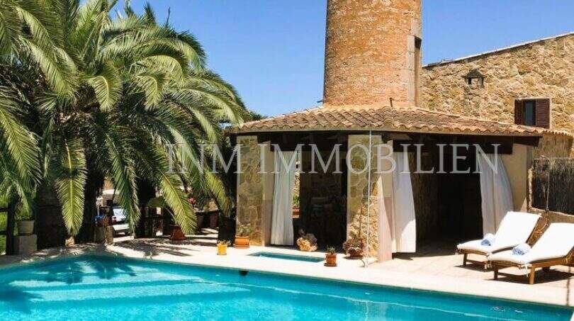 Pool mit Sonnenliegen, Palmen und historischem Steinturm einer rustikalen Finca in S'Aranjassa, Palma