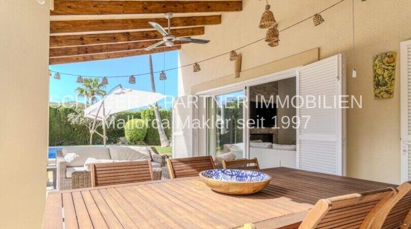 Überdachte Terrasse mit Holztisch, Deckenventilator und Blick auf den Gartenbereich der mediterranen Villa in Sa Coma.