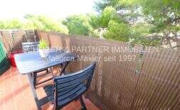 Sunny terrace with garden furniture and privacy screen, surrounded by pine trees, of the 4-room apartment in Porto Cristo.