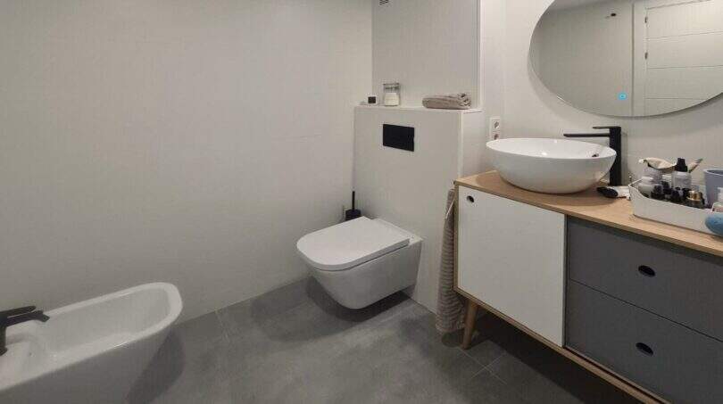 Modernes Badezimmer des Penthouses in Portitxol mit Bidet, Wand-WC, Waschtisch und ovalem Spiegel.