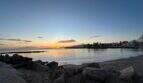 Sonnenuntergang über dem Meer am Strand von Portitxol, Palma de Mallorca, mit Palmen und Stadtsilhouette