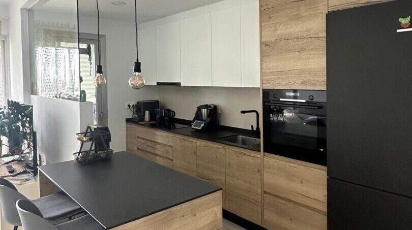 Moderne Küche mit Holzfronten, schwarzer Arbeitsplatte, Kücheninsel und Pendelleuchten im Penthouse Portitxol