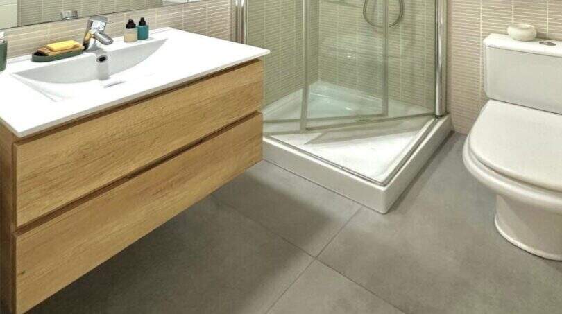Modernes Badezimmer des Penthouses mit Glasdusche, Holzwaschtisch und großformatigen Bodenfliesen in Portitxol