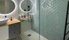 Modernes Badezimmer mit Walk-in-Dusche, mintfarbenen Fischgrät-Fliesen und beleuchtetem Rundspiegel im Penthouse Portitxol