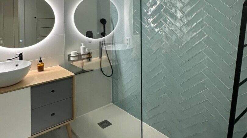 Modernes Badezimmer mit Walk-in-Dusche, mintfarbenen Fischgrät-Fliesen und beleuchtetem Rundspiegel im Penthouse Portitxol