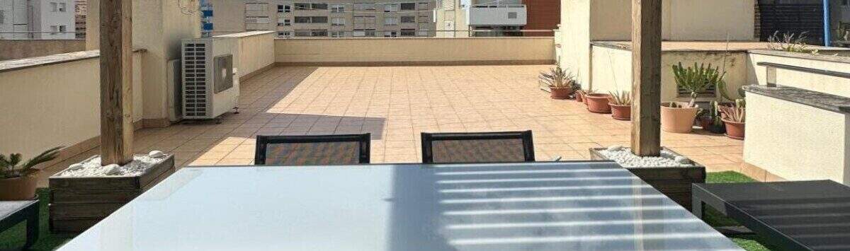 Dachterrasse des Penthouses in Portitxol mit Pergola, Lichterketten, türkisen Stühlen und Blick über Palma de Mallorca.
