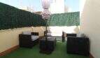 Dachterrasse des Penthouses mit Kunstrasenboden, schwarzen Rattanmöbeln, weißen Polstern und Sonnenschirm in Palma