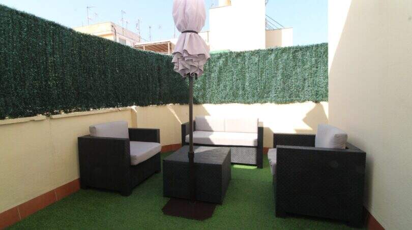 Dachterrasse des Penthouses mit Kunstrasenboden, schwarzen Rattanmöbeln, weißen Polstern und Sonnenschirm in Palma