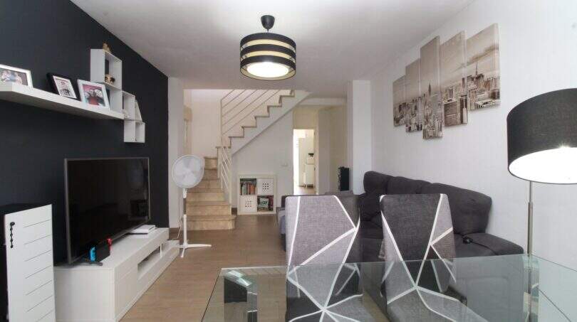 Helles Wohnzimmer der Maisonette in Palma mit grauer Couch, TV-Wand und Treppenaufgang zum Obergeschoss.