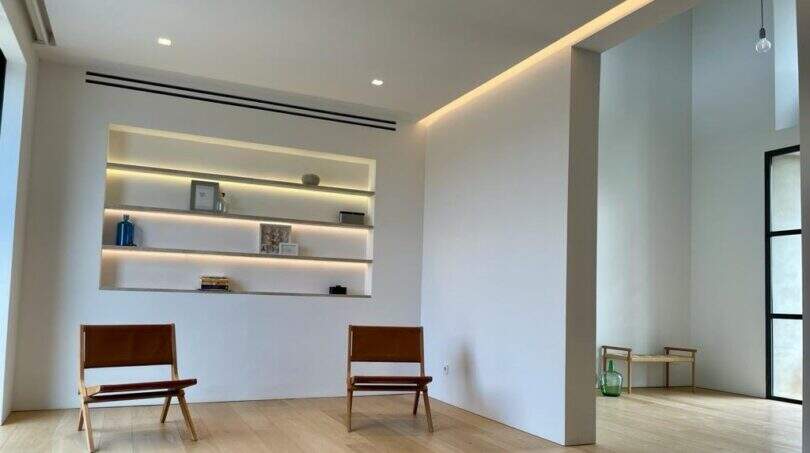 Minimalistisches Wohnzimmer mit Ledersesseln, beleuchtetem Einbauregal und Holzboden im eleganten Anwesen Marratxí.