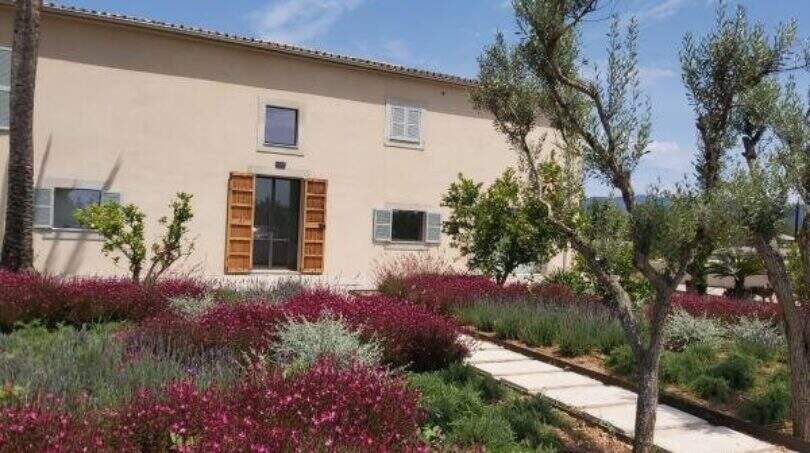 Elegantes Anwesen in Marratxí mit mediterranem Garten, Olivenbäumen und blühenden Sträuchern vor hellem Landhaus.