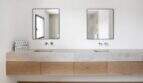 Modernes Doppelwaschbecken aus Naturstein mit Holzunterschrank und zwei Spiegeln in elegantem Badezimmer.