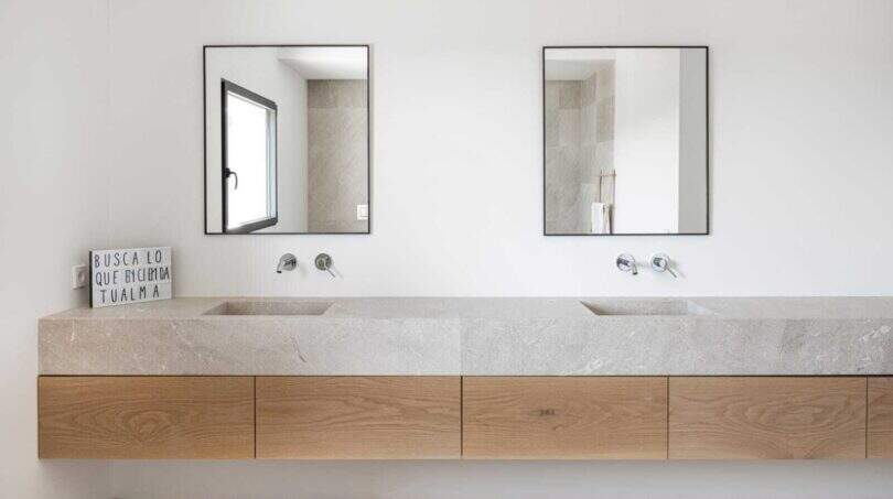 Modernes Doppelwaschbecken aus Naturstein mit Holzunterschrank und zwei Spiegeln in elegantem Badezimmer.