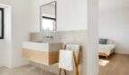Modernes Badezimmer mit Natursteinwaschbecken, Holzunterschrank und Handtuchständer, angrenzend an helles Schlafzimmer.
