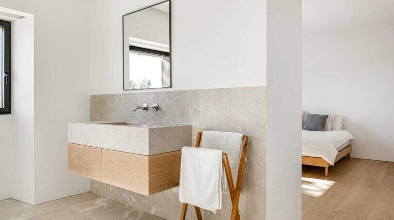 Modernes Badezimmer mit Natursteinwaschbecken, Holzunterschrank und Handtuchständer, angrenzend an helles Schlafzimmer.
