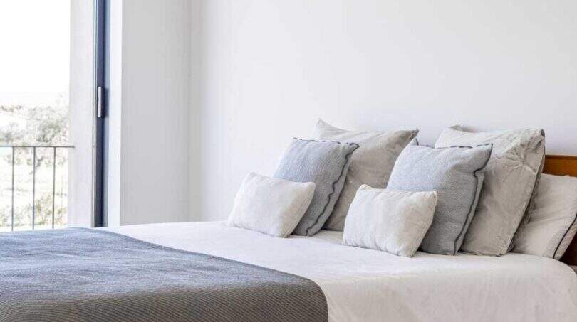 Helles Schlafzimmer mit Holzbett, grauer Tagesdecke, weißen Wänden und Balkontür in Anwesen Marratxí