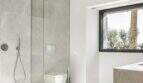 Modernes Badezimmer mit Regendusche, Glastrennwand, Wand-WC und Natursteinoptik in Anwesen Marratxí.