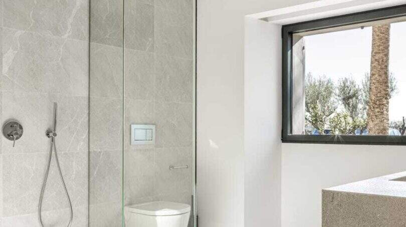 Modernes Badezimmer mit Regendusche, Glastrennwand, Wand-WC und Natursteinoptik in Anwesen Marratxí.