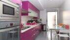Modern kitchen with striking pink built-in cabinets, stainless steel appliances and dining table in ground floor apartment Palma