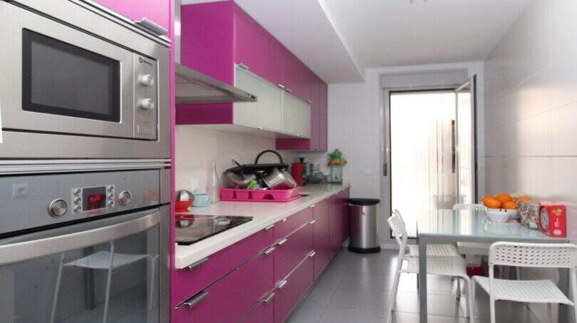 Modern kitchen with striking pink built-in cabinets, stainless steel appliances and dining table in ground floor apartment Palma