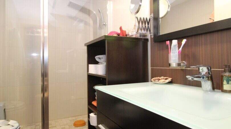 Modern bathroom of the ground floor apartment in Palma with glass shower, dark sink and wall mirror.