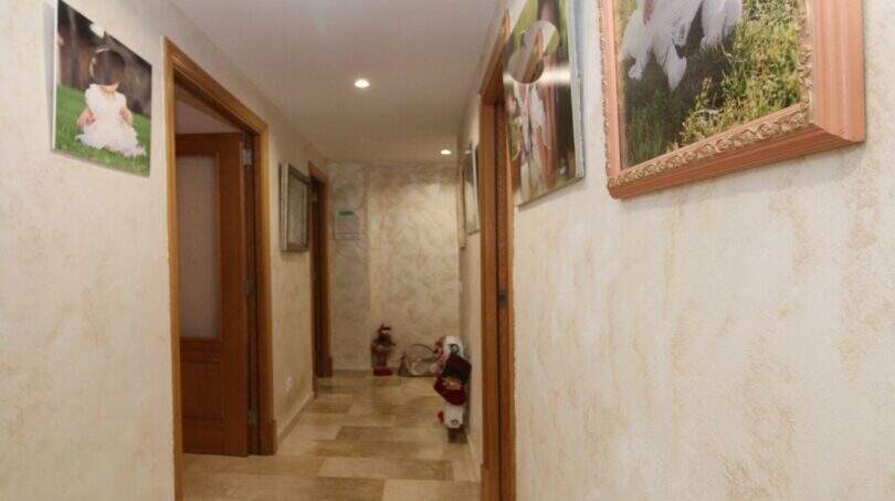 Bright hallway of the ground floor apartment in Palma with marble floor, wooden doors and family photos on the wall.