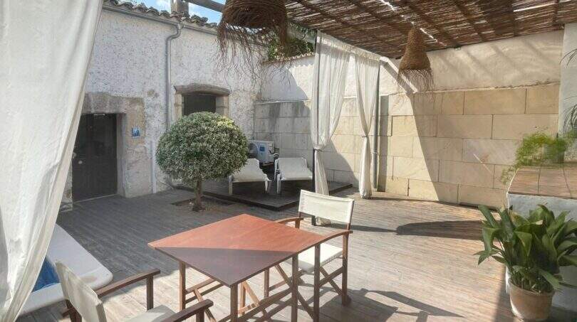 Terraza cubierta con tarima de madera, mesa de comedor, área de lounge y muros de piedra natural de la casa de pueblo en Sencelles.