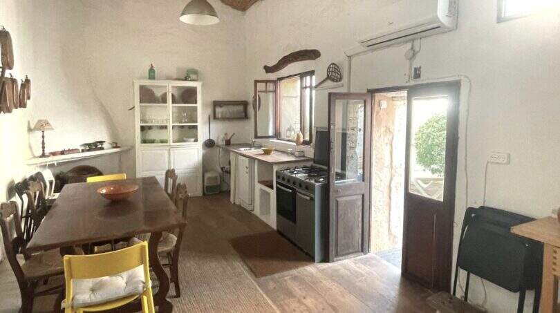 Cocina-salón rústica con techo de paja, mesa de madera, sillas amarillas y estufa de gas en la casa de pueblo Sencelles.