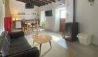 Wohnzimmer mit Ledersofa, Holzofen, Couchtisch und Essbereich, rustikale Holzbalkendecke, Sencelles Stadthaus