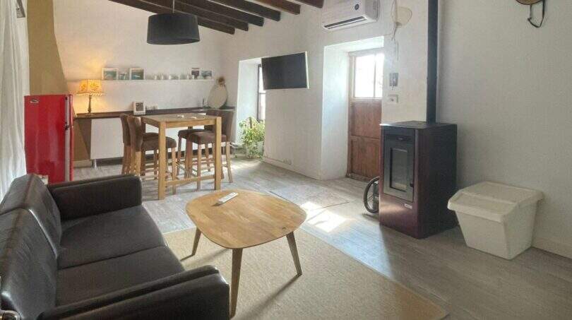 Sala de estar con sofá de cuero, estufa de leña, mesa de centro y comedor, techo rústico de vigas de madera, casa de pueblo Sencelles