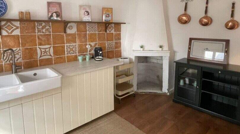 Cocina rústica con azulejos de terracota, fregadero de granja, sartenes de cobre y chimenea decorativa en la casa de pueblo Sencelles.