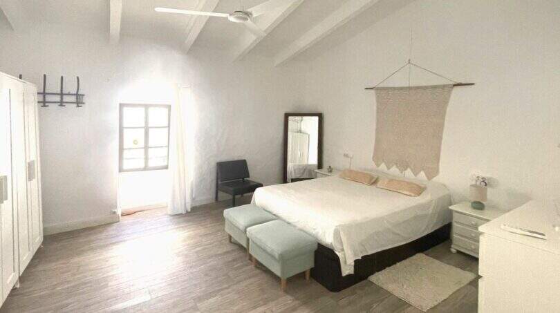 Dormitorio luminoso con cama doble, decoración de pared de macramé, suelo de madera y ventilador de techo en la casa de pueblo Sencelles