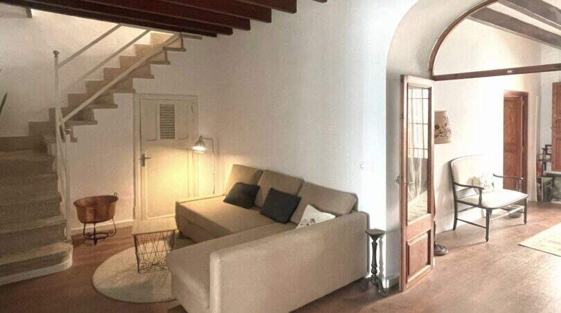 Sala de estar con techo de vigas de madera, abertura de arco, sofá y escaleras en la casa de pueblo Sencelles
