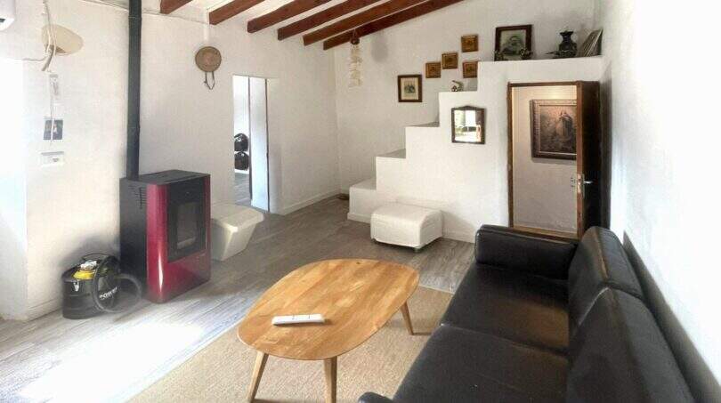 Sala de estar con techo de vigas de madera, estufa de pellets, sofá de cuero y escaleras en la casa de pueblo Sencelles