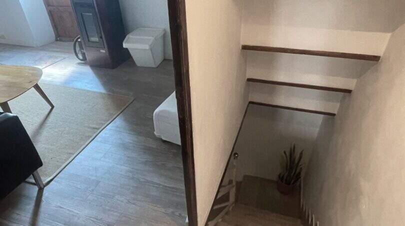 Escalera con paredes blancas y peldaños de madera, vista a la sala de estar con estufa de leña en la casa de pueblo Sencelles.