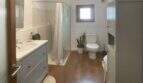 Helles Badezimmer mit grauem Waschtisch, Dusche, WC und Holzboden im Stadthaus Sencelles.