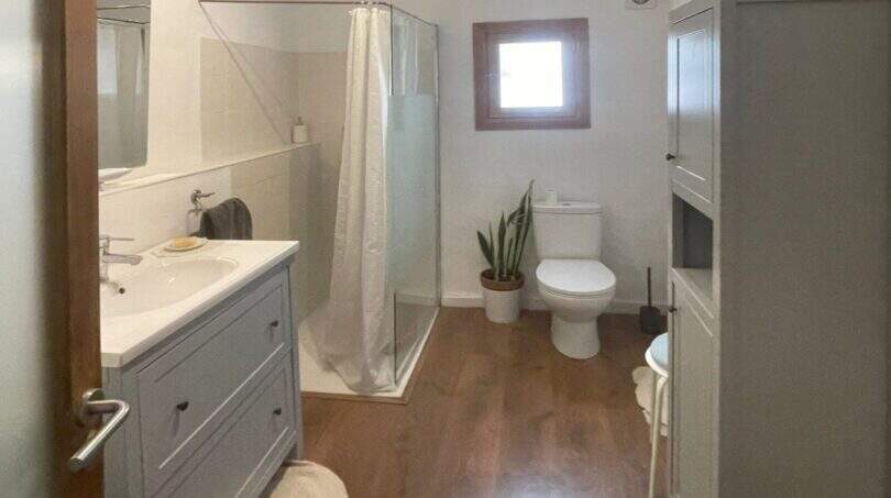 Baño luminoso con lavabo gris, ducha, WC y suelo de madera en la casa de pueblo Sencelles.