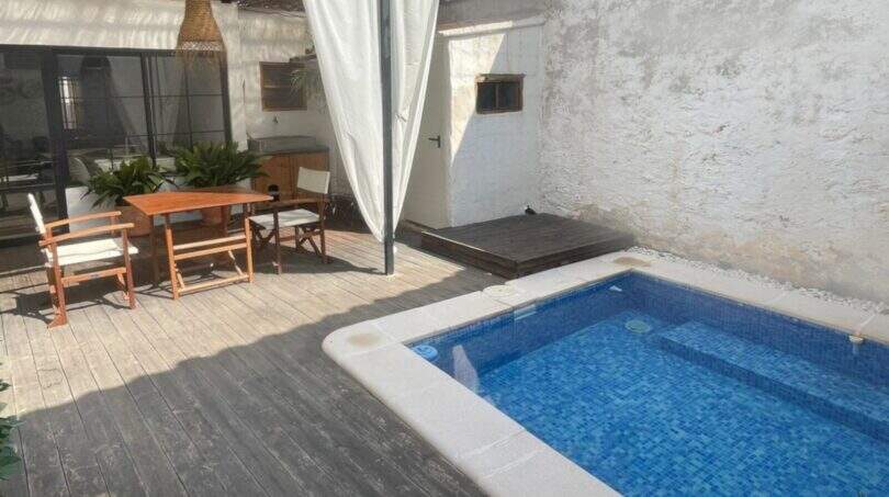 Terraza soleada con tarima de madera, piscina de mosaico azul y zona de comedor cubierta en Sencelles